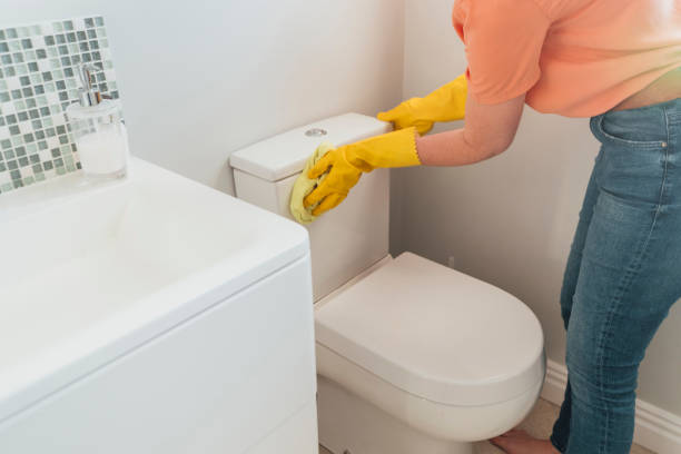 An adult wearing protective yellow gloves cleans the toilet with a sponge.
